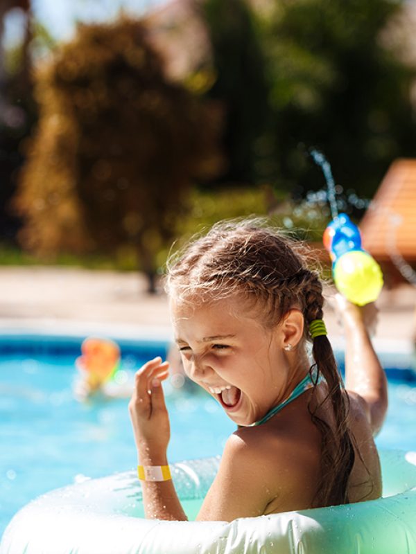 Cheerful children playing waterguns, rejoicing, jumping, swimming in pool. Copy space