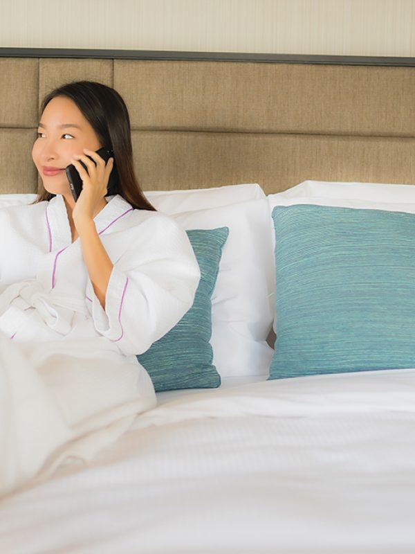 Portrait beautiful young asian women using mobile smart phone with coffee cup on bed in bedroom interior